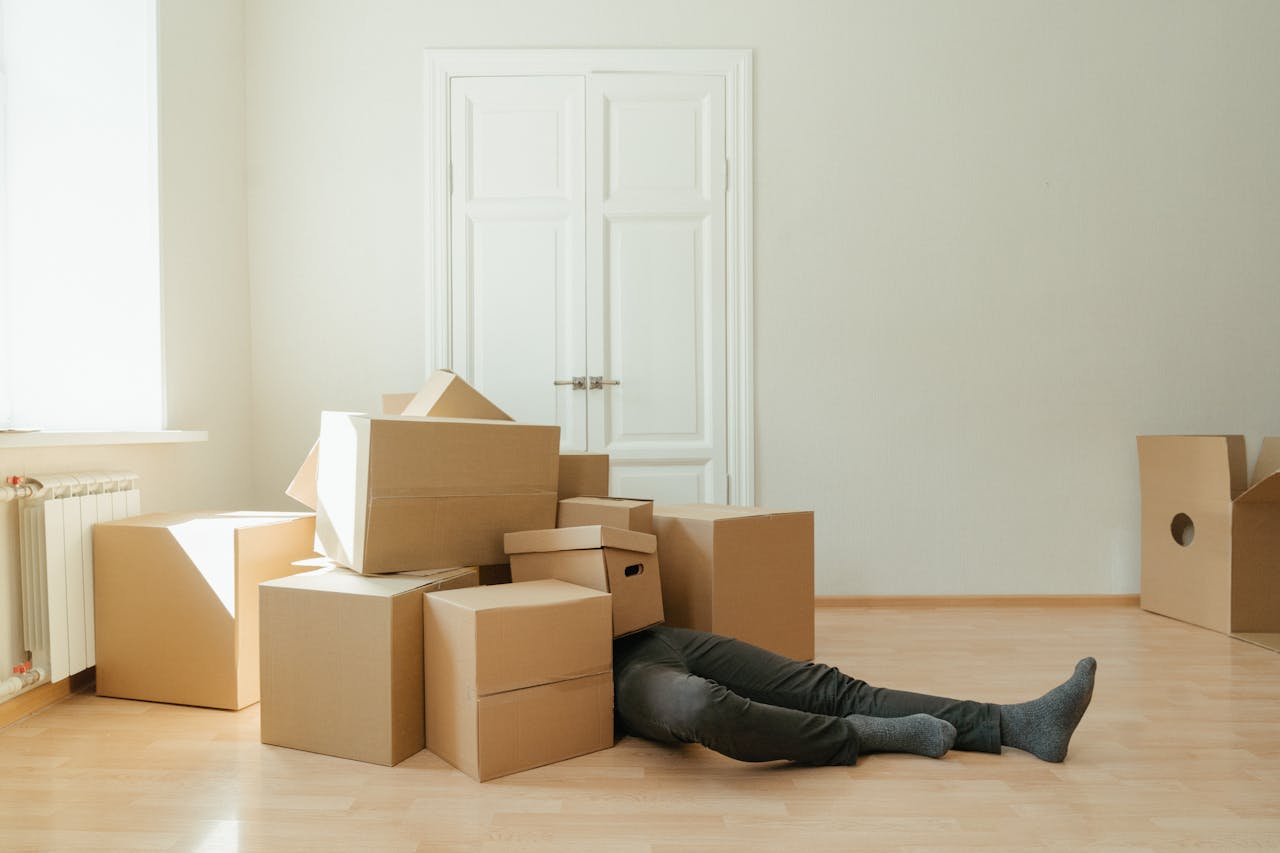 Person on floor surrounded by cardboard boxes during moving; concept of stress and relocation.